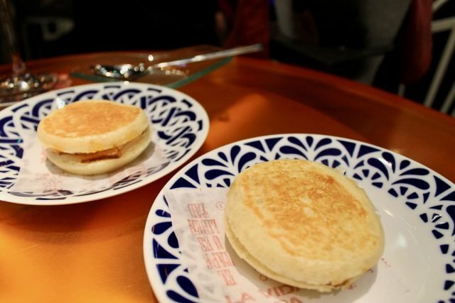 Dos mini bocadillos de pan blando servidos en platos de loza azul y blanca sobre la barra de Tickets