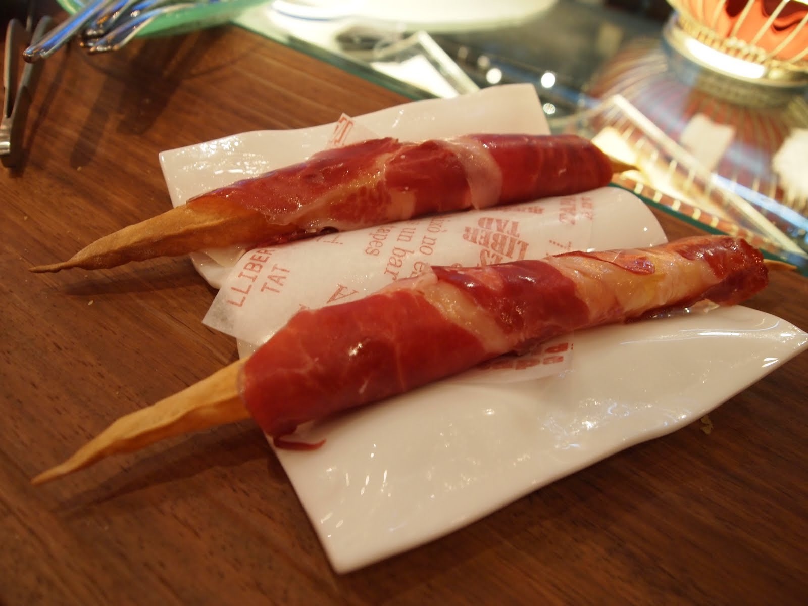 Dos picos de pan crujiente envueltos en jamón ibérico sobre una servilleta de papel de Tickets